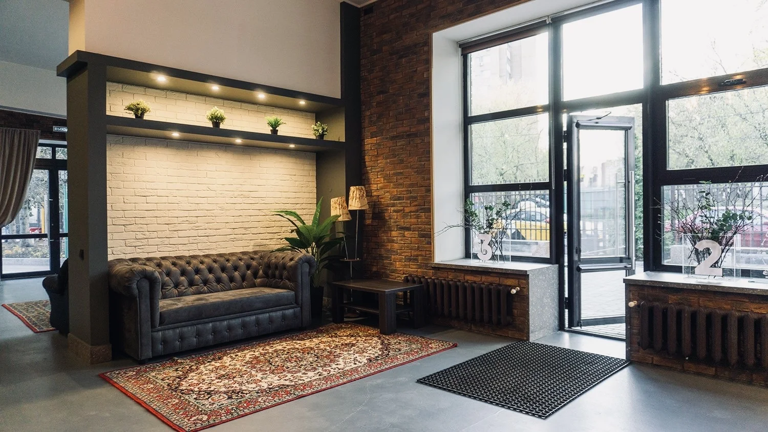 Входная зона 314 Loft — диван Честерфилд, белая кирпичная ниша с растениями, большие окна
